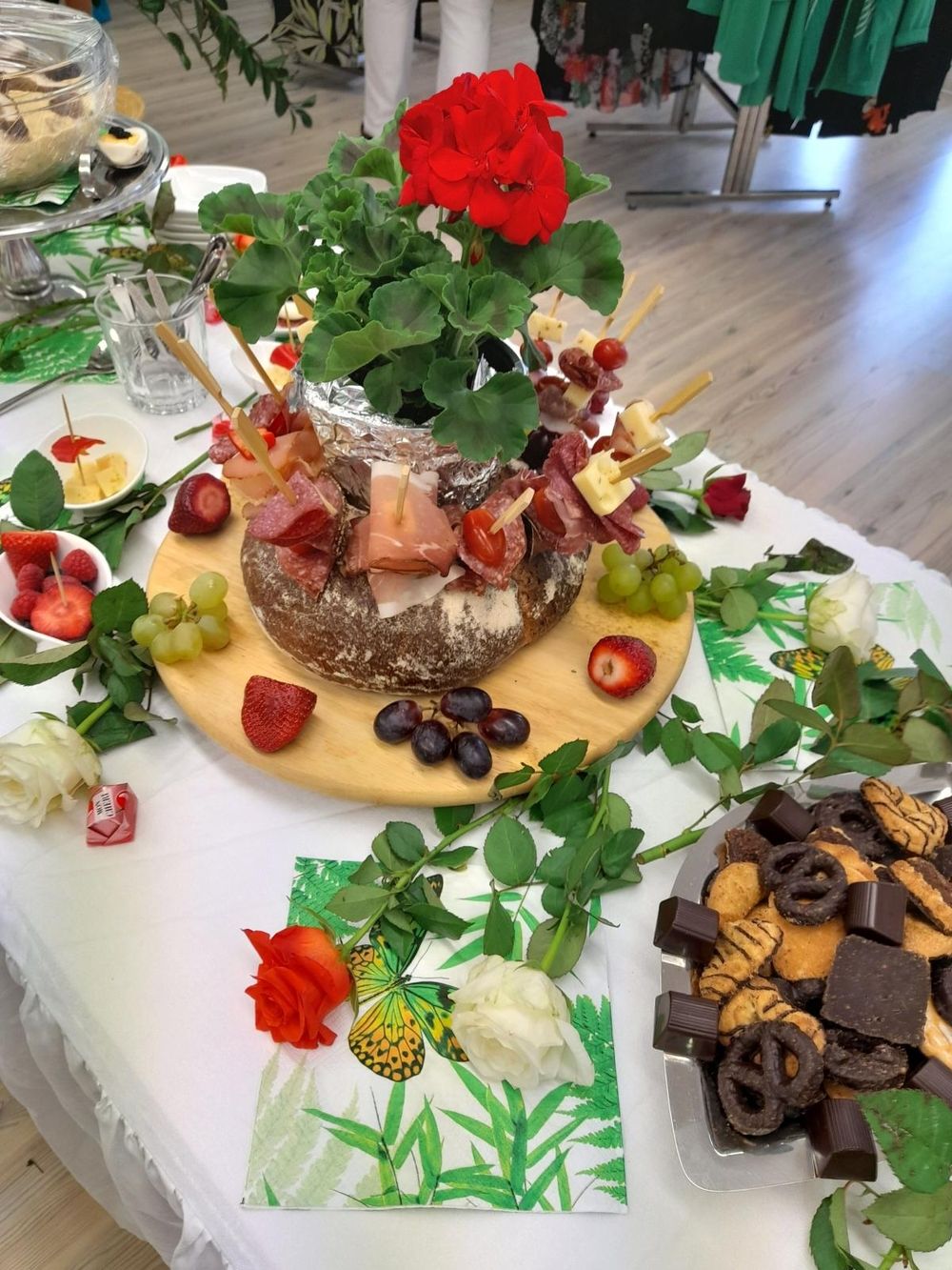 Ein Buffettisch mit Käse- und Fleischspießen, Obst und verschiedenen Süßigkeiten, umgeben von Blumen.